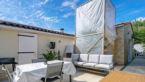 Une terrasse avec une table et des chaises, un canapé et un petit bâtiment à la façade en pierre.