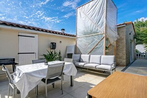 A patio with a table and chairs, a sofa, and a small building with a stone facade.