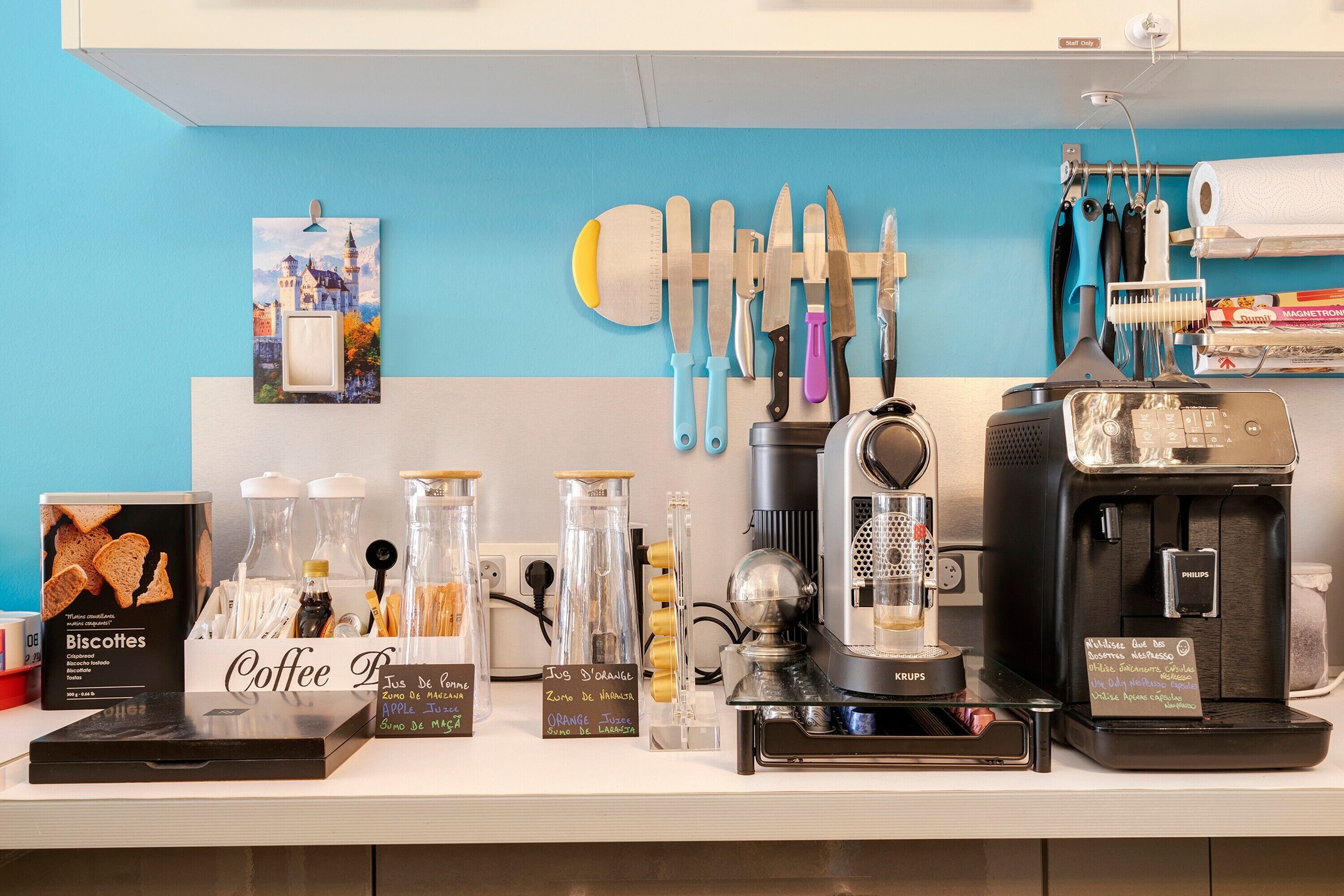 Una estación de café con una cafetera, un cartel con los sabores de café y un soporte de cuchillos en la pared.