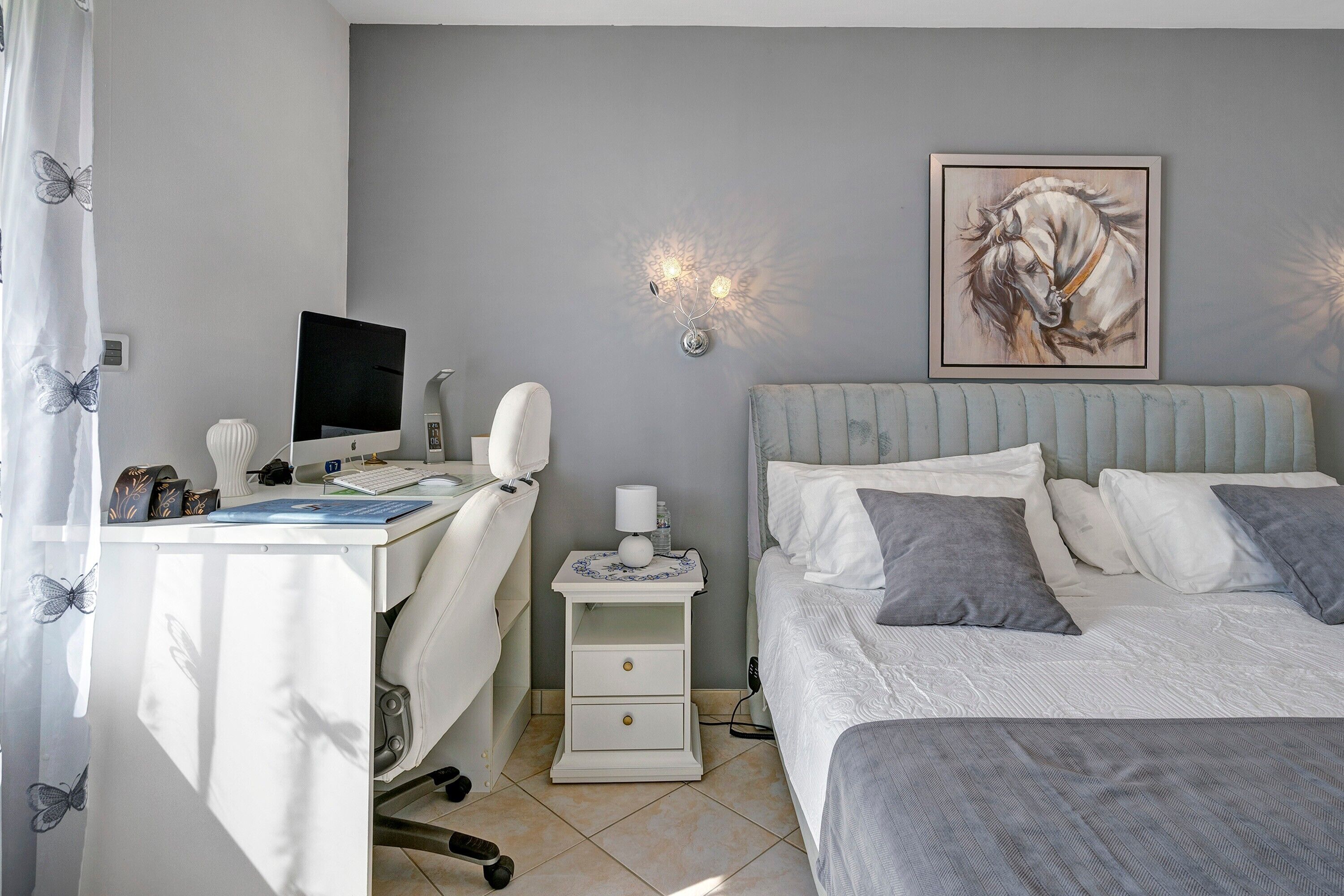 Ein Schlafzimmer mit Bett, Nachttisch, Schreibtisch inklusive Computer und einer Wandlampe.