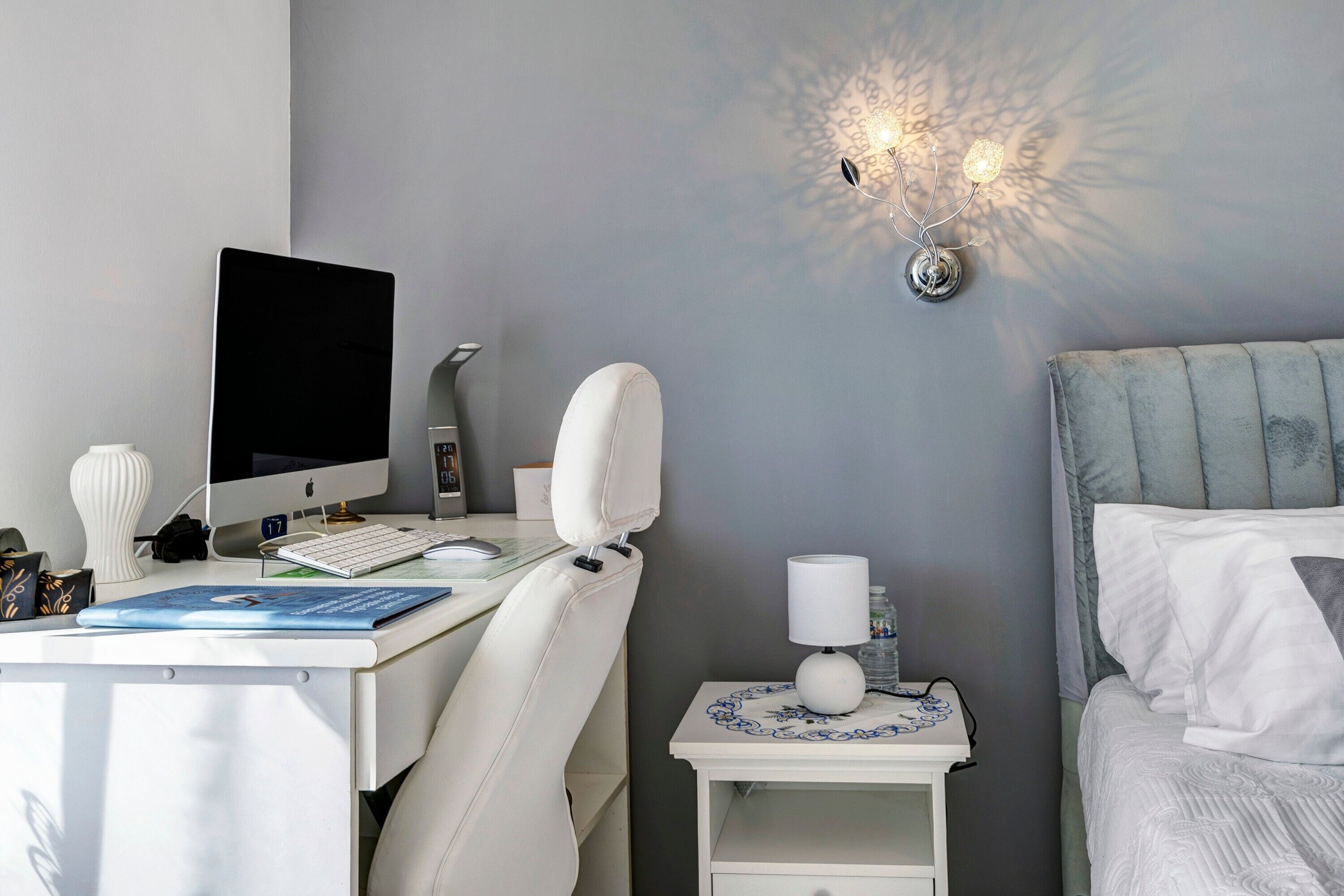Quarto moderno com escrivaninha, computador, luminária e cama.