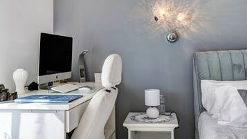 Quarto moderno com escrivaninha, computador, luminária e cama.