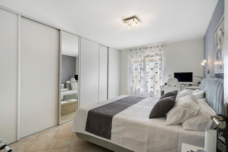 A modern bedroom with a bed, a desk, and a television.. Gîte “Les Lauriers Roses Du 17” with Private Terrace, Wi-Fi, and Air Conditioning