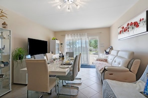 Una sala de estar moderna con comedor, televisor de pantalla plana, sofá y mesa de comedor para cuatro.