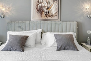 Un lit avec une literie blanche et grise, une tête de lit grise et deux appliques murales.
