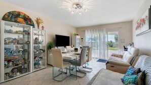 Un vaste espace de vie comprenant une table à manger, des chaises, un canapé, un téléviseur et une vitrine contenant des objets décoratifs.