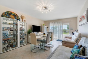 A spacious living area with a dining table, chairs, a sofa, a TV, and a glass cabinet with decorative items.