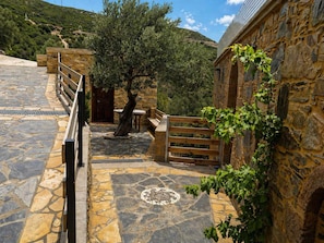 A stone pathway leading to a building with a wooden gate, a tree, and a stone table. - Harmony House- Sea View Cretan Escape With Jacuzzi (Kissamos)