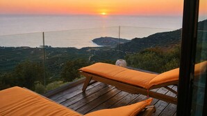 A balcony with a wooden floor and two orange cushioned chairs, overlooking a coastal landscape with a sunset. - Harmony House- Sea View Cretan Escape With Jacuzzi (Kissamos)