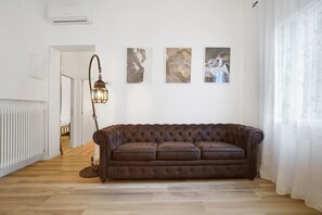 A room with a brown leather sofa, a floor lamp, and three framed artworks on the wall. - Airoldi Palace Apartment: Comfort Between Sea and City (Chioggia)