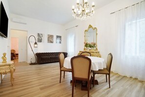 En spisestue med lysekrone, et rundt bord med stole, en sofa og et spejl.