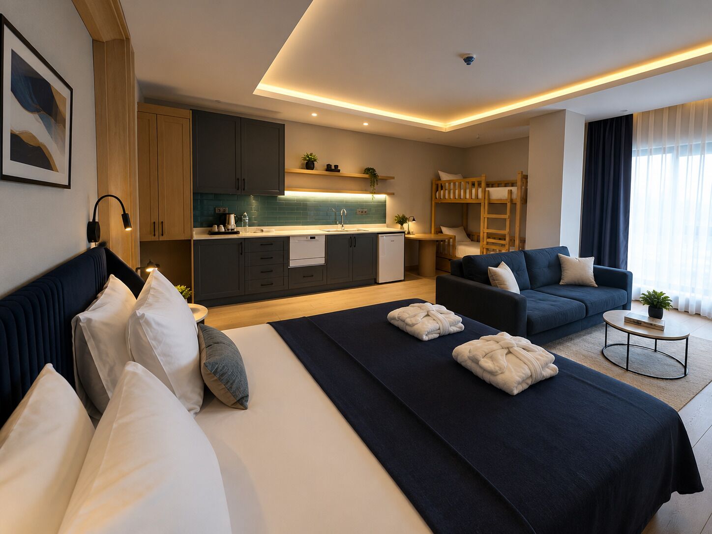 A modern hotel room with a bed, a sofa, a small kitchen, and a bunk bed.