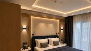 Una habitación de hotel moderna con una cama grande, lámparas de noche, una mesita y un teléfono en la mesita de noche.