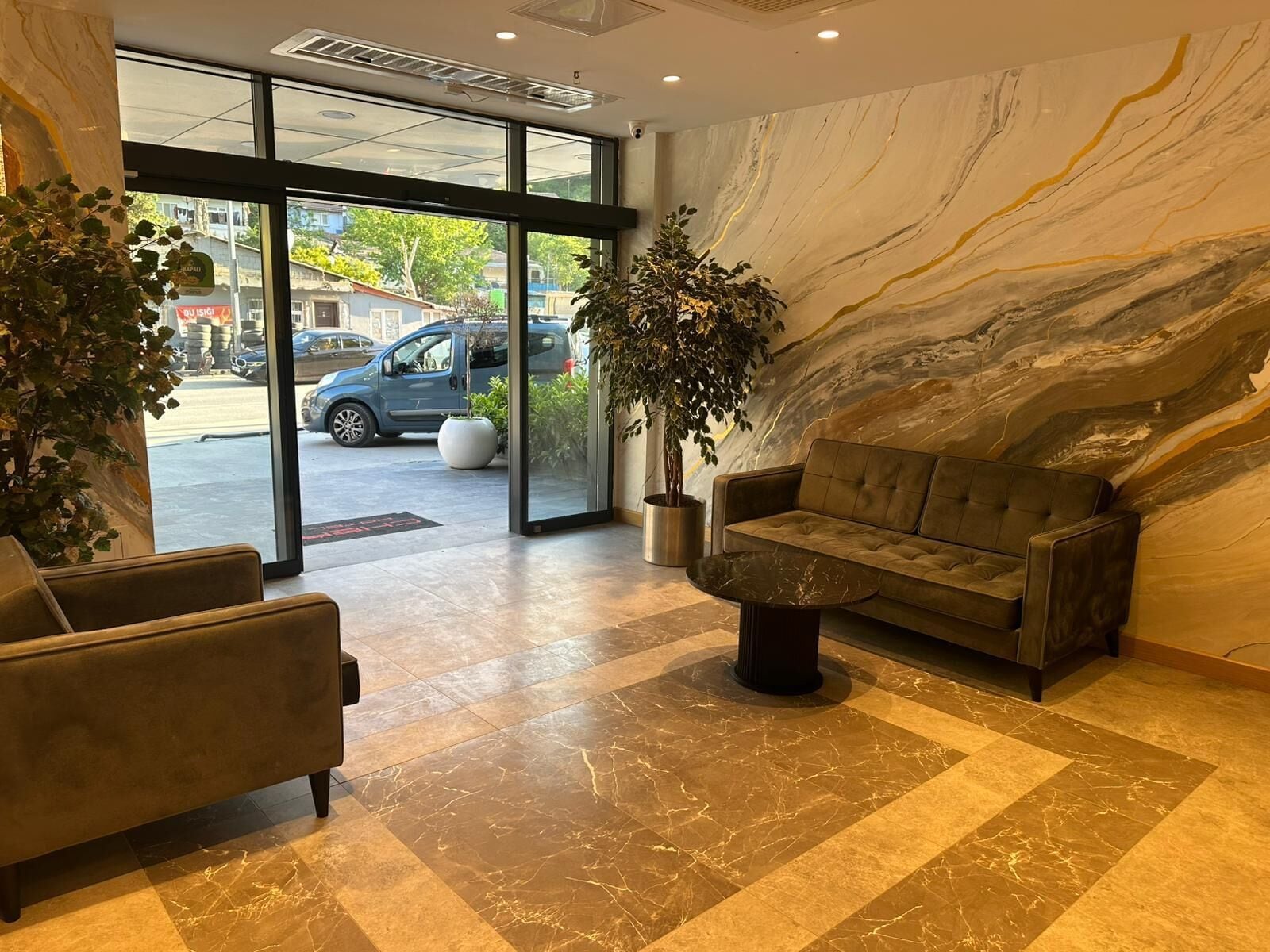 A lobby with a sofa, chairs, a coffee table, a marble wall, and a large window with a view of the street.