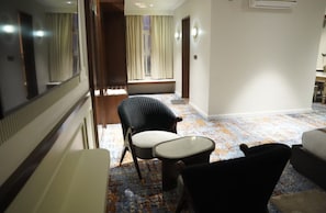 A hotel hallway with a patterned carpet, a seating area with a chair and a small table, and a mirror on the wall. - Vijay Villas Rathara - Silpara Bypass Rd (Huzur)