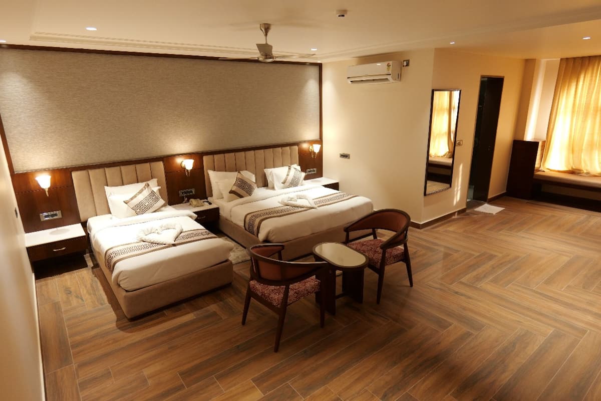 Habitación de hotel con dos camas, una mesita pequeña, dos sillas, ventilador de techo, aire acondicionado y un espejo grande.