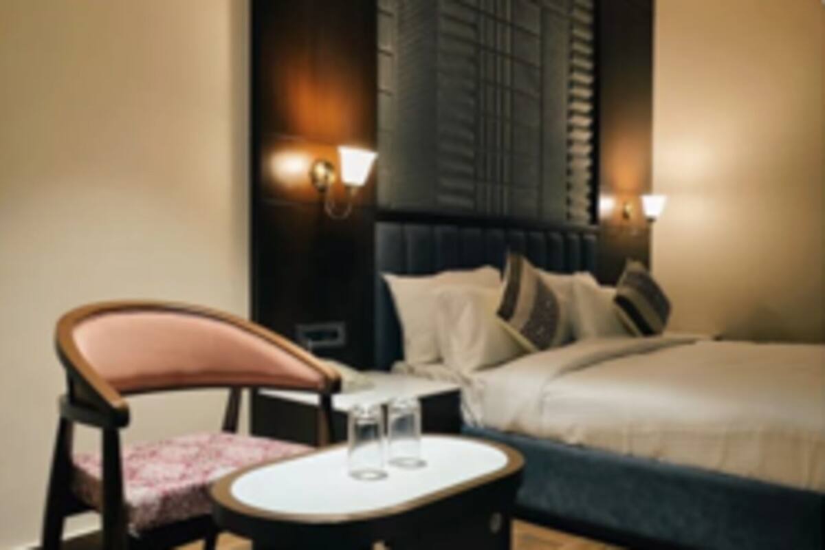 Una habitación de hotel con una cama, una silla, una mesita y lámparas fijadas a la pared.