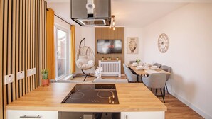 Uma cozinha moderna com uma ilha central, uma área de jantar com mesa e cadeiras, uma cadeira pendente e uma TV fixada na parede.