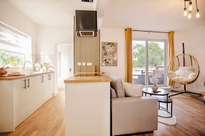 Eine moderne Küche mit Kochinsel, Essbereich mit Sofa und Sessel, und großes Fenster mit Vorhängen.