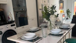 A modern kitchen with a dining table set for four, a refrigerator, oven, and washing machine. - Beautiful London City Home (London)