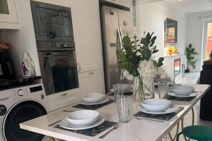 A modern kitchen with a dining table set for four, a refrigerator, oven, and washing machine. - Beautiful London City Home (London)