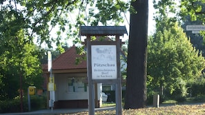 A sign for 'Pötzschau' with a depiction of a village scene, a red-roofed building, and a tree in the background. - Apartment 'Für 3 Personen 63 M²' (Rötha)