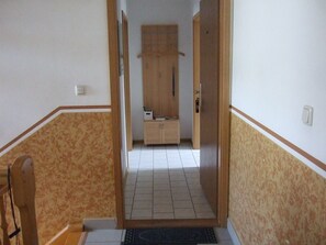 Ein Korridor mit einer Holztür, die in einen Raum führt, einem kleinen Schrank und einem Stuhl.