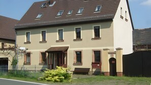 A two-story building with a sloped roof, multiple windows, and a front entrance with a door. - Apartment 'Für 3 Personen 50 M²' with Shared Garden (Rötha)