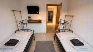 A twin room with two beds, a TV mounted on the wall, a small shelf with a plant, and a hallway leading to another room. - Apartment 'Control Suites Og Rechts' with Private Terrace and Wi-Fi (Urbar)