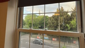 Una ventana con vistas a una carretera y árboles, un edificio con una aguja y una señal de calle.