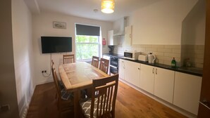 Una cocina moderna con armarios blancos, una mesa de comedor de madera y un televisor de pantalla plana montado en la pared.
