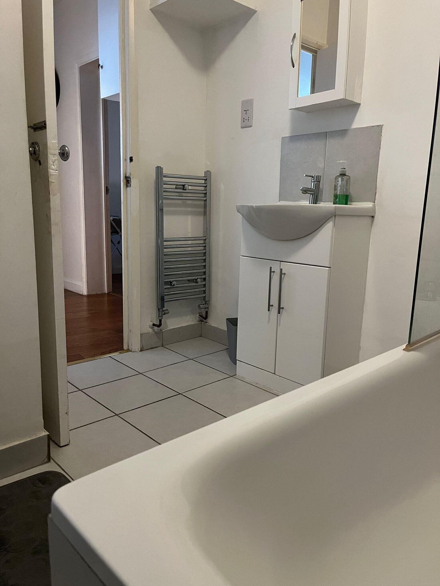 Een badkamer met een wit wastafelmeubel, spiegel, en kast, een handdoekhouder, en een douchegedeelte.