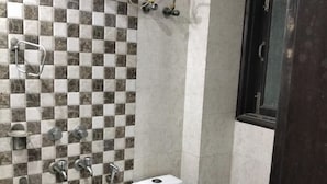 A bathroom with a checkered tile wall, a toilet, a shower, and a sink. - Staylo The Starlight Inn (New Delhi)