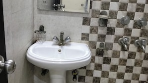 A bathroom with a white pedestal sink, a mirror, a towel rack, and a tiled wall with a checkered pattern. - Staylo The Starlight Inn (New Delhi)