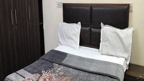 A bed with a floral bedspread, a dark headboard, and white pillows. - Staylo The Starlight Inn (New Delhi)