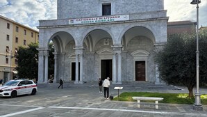 A historic building with a prominent entrance, a sign indicating it is the Cattedrale di Livorno, and a statue in front.