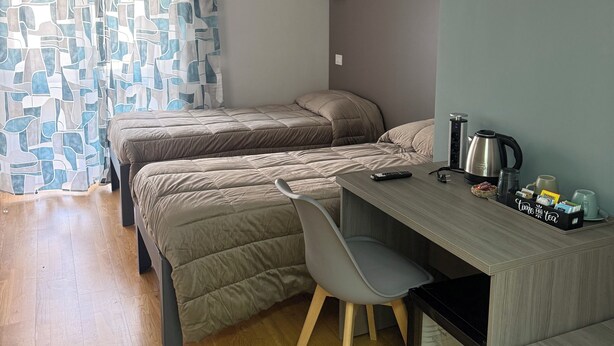 A compact room with two beds, a desk with a chair, a kettle, and a framed picture on the wall.