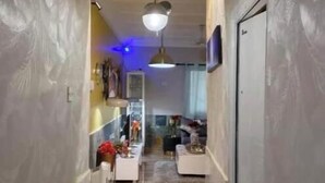 A hallway leading to a dining area with a ceiling fan, a TV mounted on the wall, and a wooden floor. - Home Away From Home - Calm & Stylish Retreat for a Relaxing Stay (Koforidua)