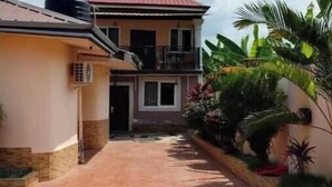 A two-story house with a red roof, a balcony, and a paved driveway. - Home Away From Home - Calm & Stylish Retreat for a Relaxing Stay (Koforidua)