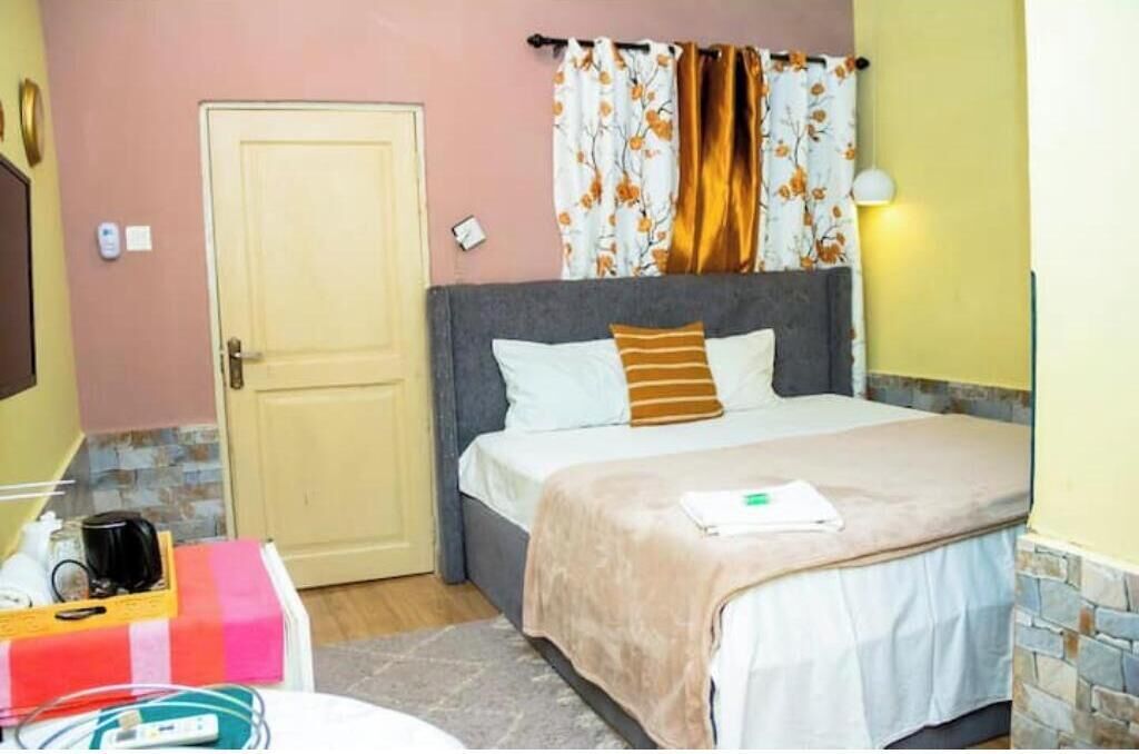 A bedroom with a bed, a bedside table, a lamp, a door, and a window with curtains.