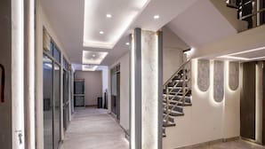 Un pasillo moderno con suelo de mármol, puertas de cristal, una escalera con barandilla de metal e iluminación empotrada.