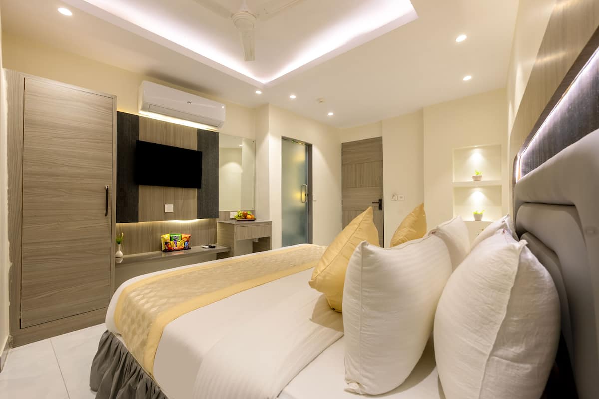 A modern hotel room with a large bed, a flat-screen TV, a vanity, and a walk-in closet.