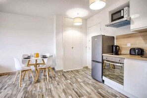 Une cuisine moderne équipée d’un four à micro-ondes, d’un réfrigérateur et d’un four encastrés. On y trouve une table à manger avec des chaises et un plancher en bois.