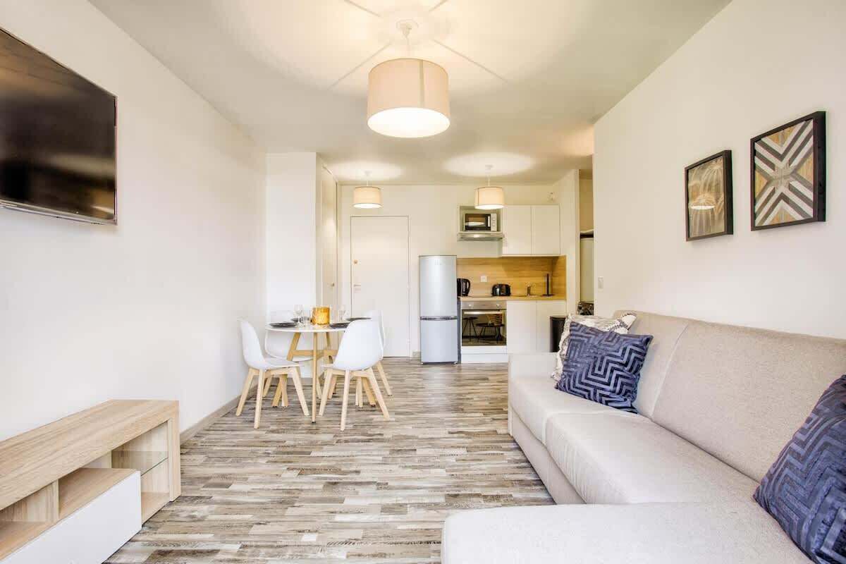 Una sala moderna con sofá, mesa de comedor, sillas y una cocina al fondo.