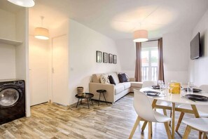 Un salon moderne comprenant un canapé, une table à manger et des chaises, un lave-linge et un téléviseur fixé au mur.