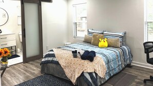 Un dormitorio con cama, ventilador de techo, ventana, silla y escritorio con un florero.