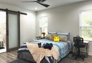 Ein Schlafzimmer mit Bett, Schreibtisch, Stuhl, Fenster und Deckenventilator.