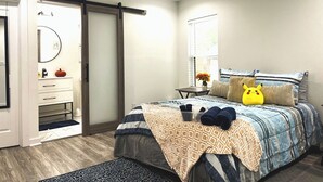 Un dormitorio con cama, ventilador de techo, cómoda, espejo, ventana y puerta.