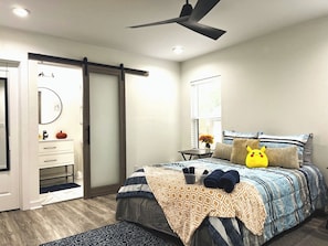 Ein Schlafzimmer mit Bett, Deckenventilator, Kommode, Spiegel, Fenster und Tür.