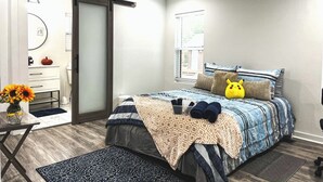 Un dormitorio con cama, almohadas, ventilador de techo, ventana y puerta.